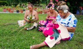 3 Frauen sitzen auf dem Boden und üben unterschiedliche Handarbeiten aus