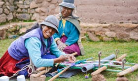 Happy native american mother and daughter weaving authentic aymara cloth.