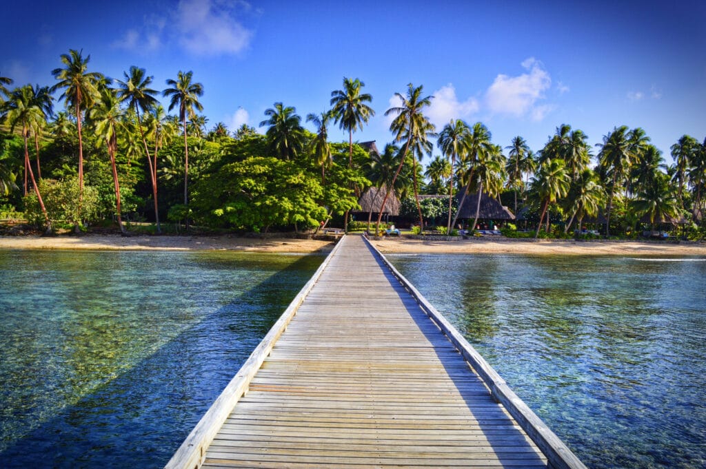Wooden pier going to paradise resort island in Fiji with palm trees on a beach