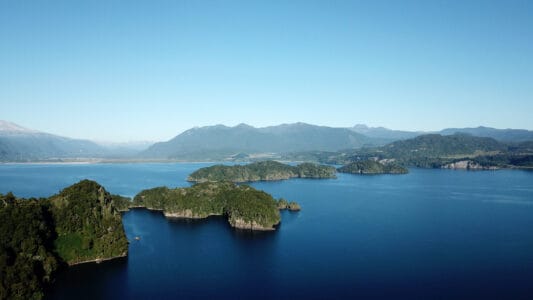 „Luftaufnahme vom See bei Puyehue in Chile mit grünen Inseln, Berglandschaft und blauem Himmel – Naturparadies für Erholung und Outdoor-Aktivitäten.“